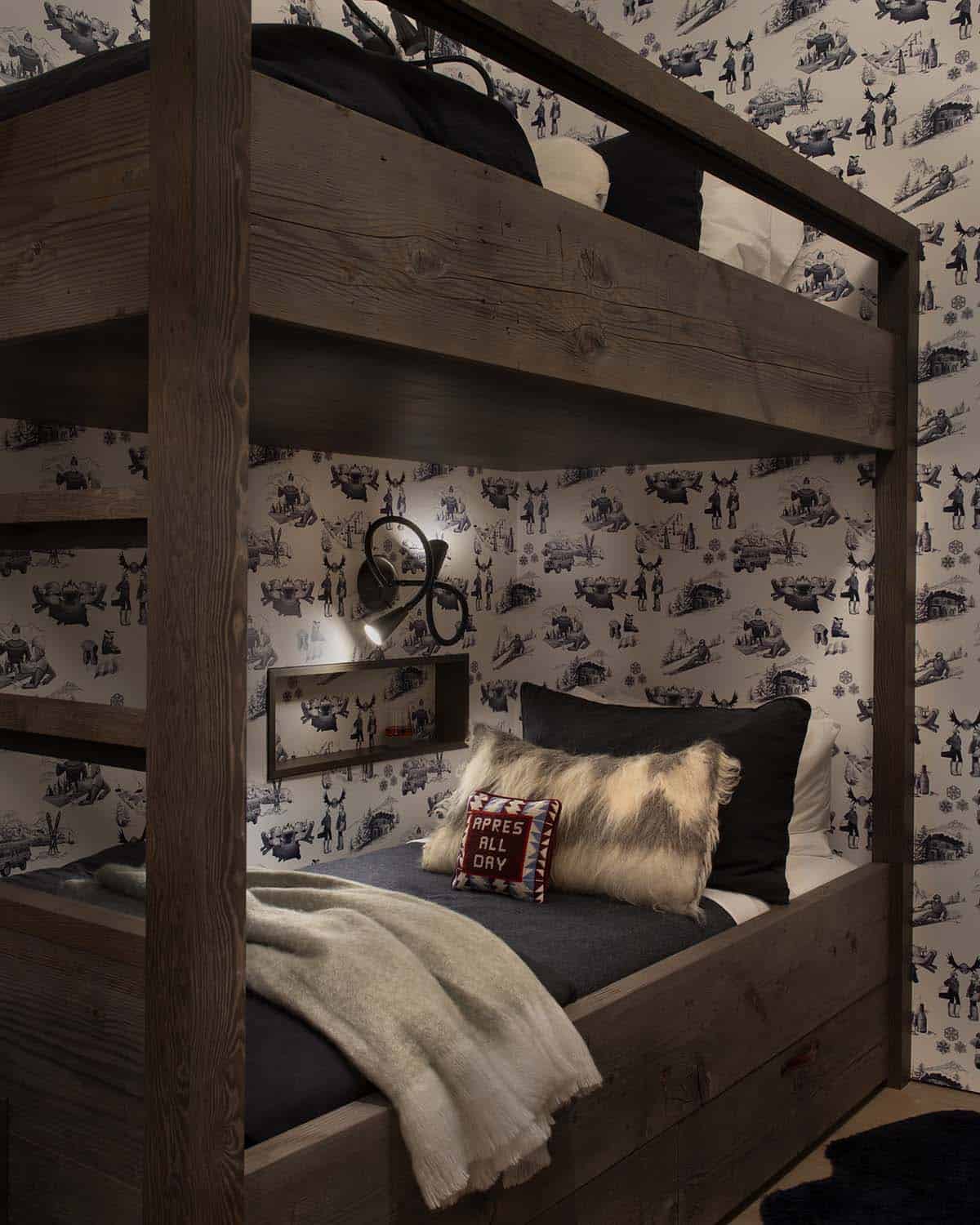 Close-up of bunk bed nook with ski toile wallpaper, fur pillow, reading light, and apres-ski cushion