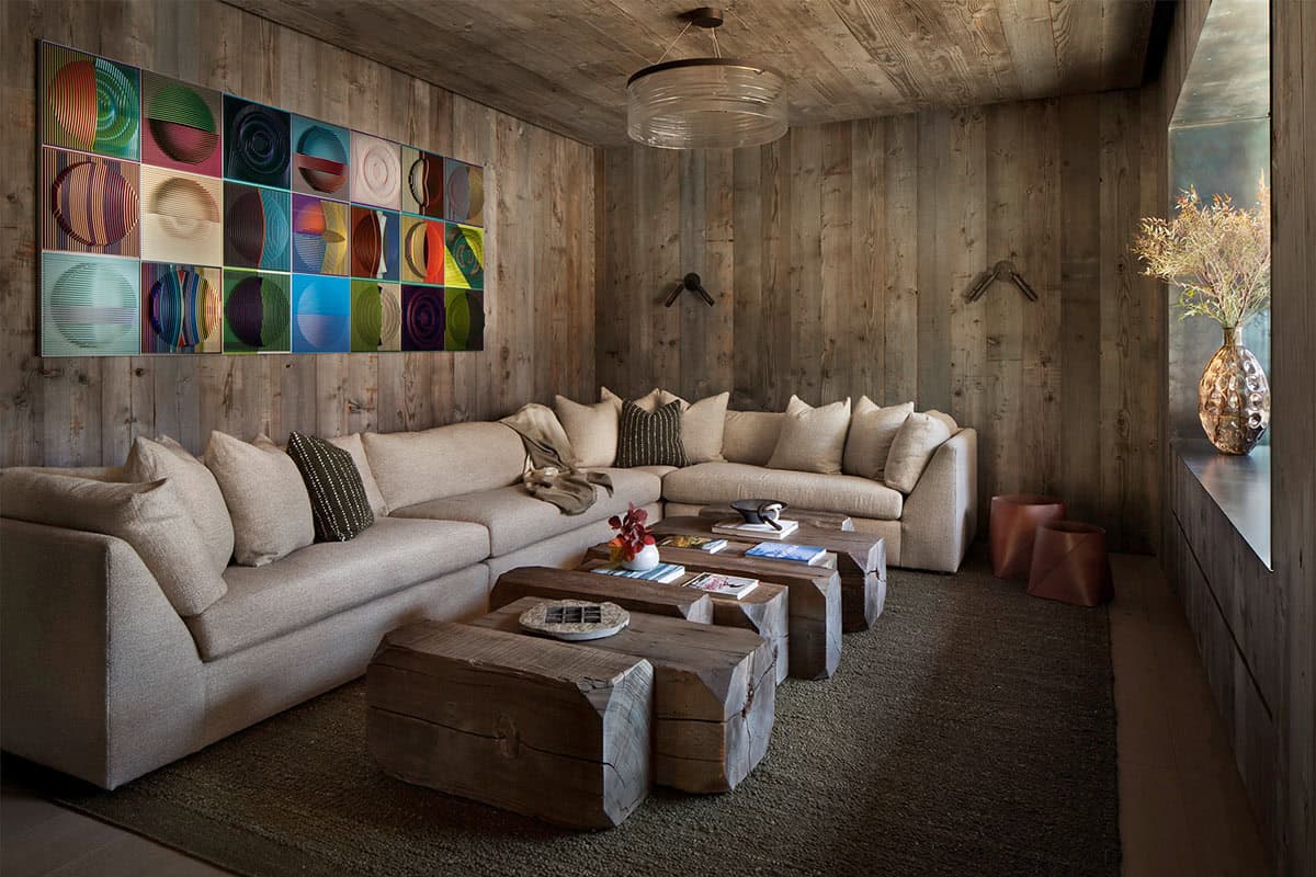Lower-level lounge with reclaimed wood walls, cream sectional, raw wood slab coffee tables, and colorful grid artwork