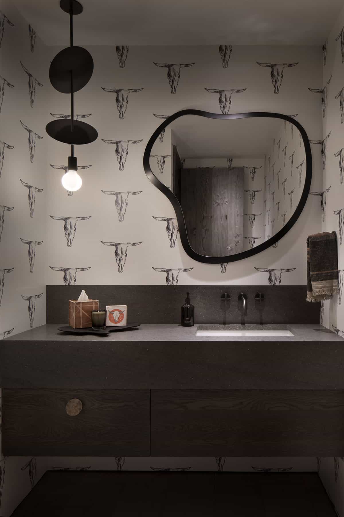 Powder room with longhorn skull wallpaper, dark wood floating vanity, organic black-framed mirror, and globe pendant