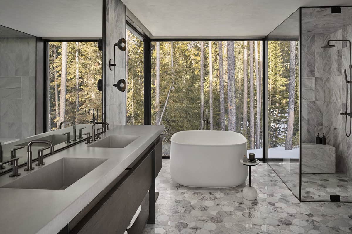 Primary bathroom with freestanding soaking tub, penny marble floor tile, double vanity, and snowy forest views