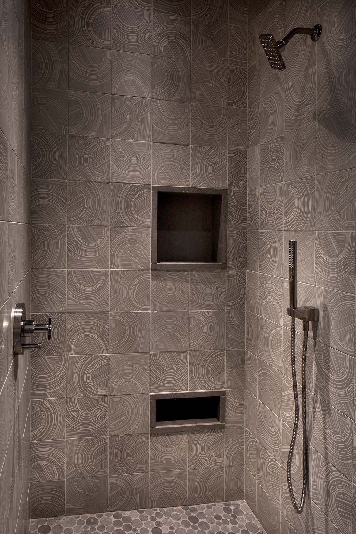 Shower interior detail with swirl-patterned ceramic tile, built-in niches, rain head, and pebble mosaic floor