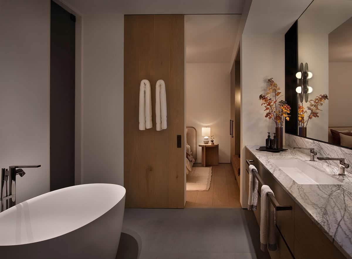 Guest bathroom with freestanding soaking tub, marble vanity, sliding oak door, and warm globe sconces