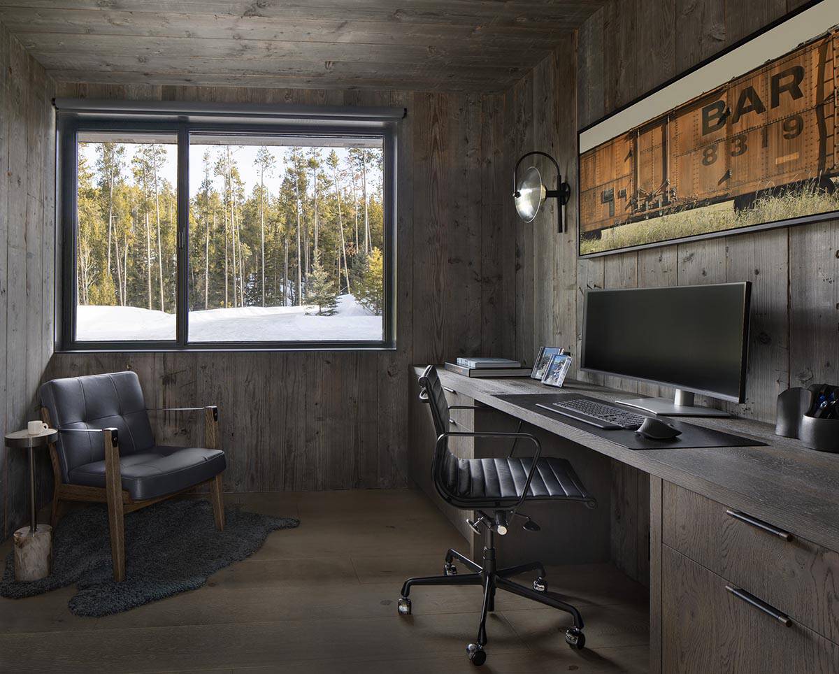 Home office with reclaimed wood walls, built-in desk, leather chair, and snowy forest window view