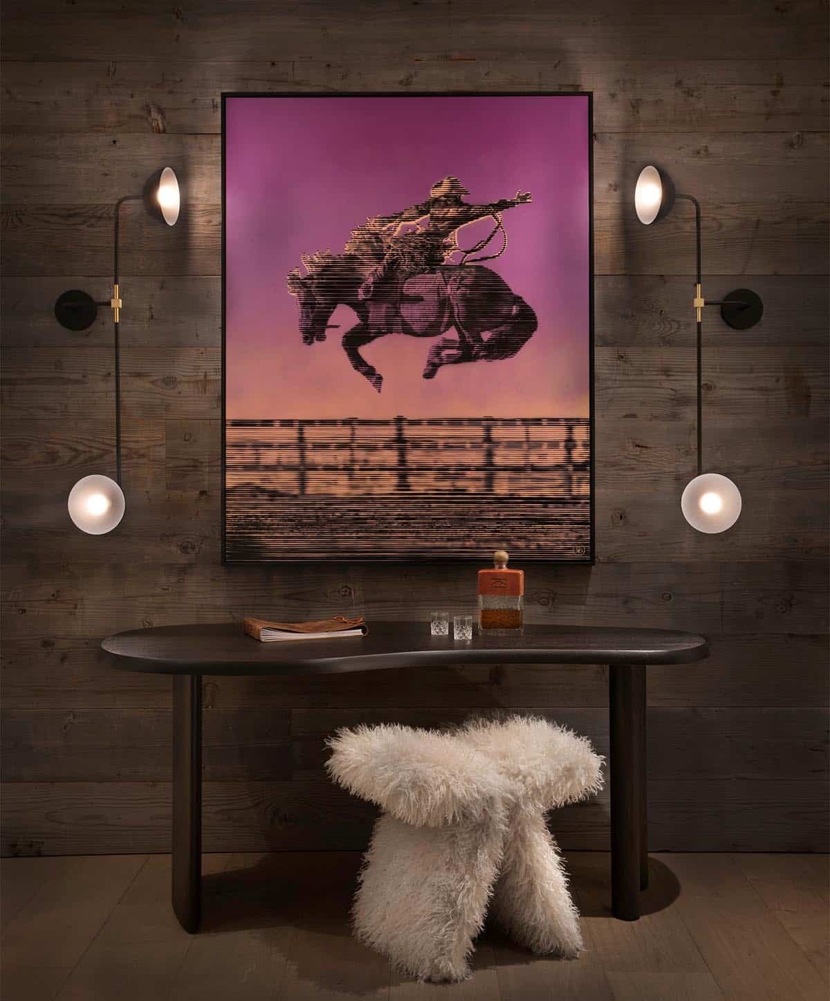 Reclaimed wood wall with large western bronco artwork flanked by four globe wall sconces and oval console table