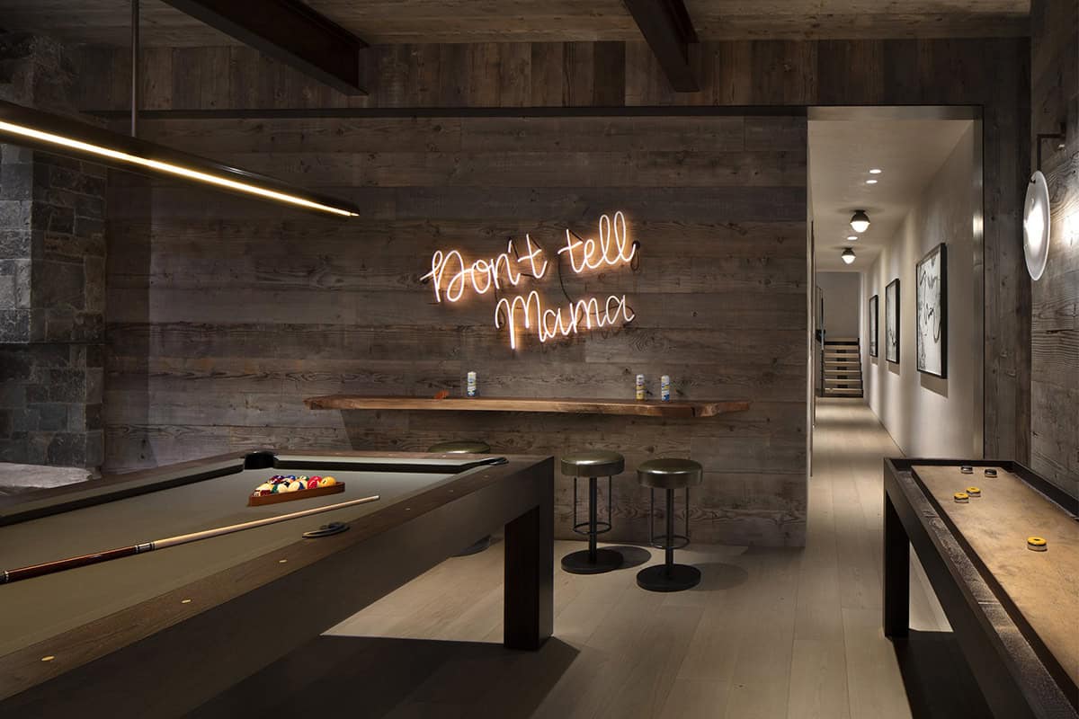 Game room with pool table, shuffleboard, neon sign, reclaimed wood walls, and gallery hallway beyond