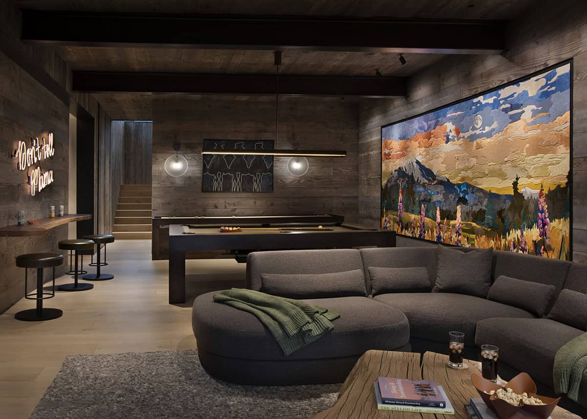 Lower-level game room with curved sectional, pool table, neon sign, and large mountain landscape wall art