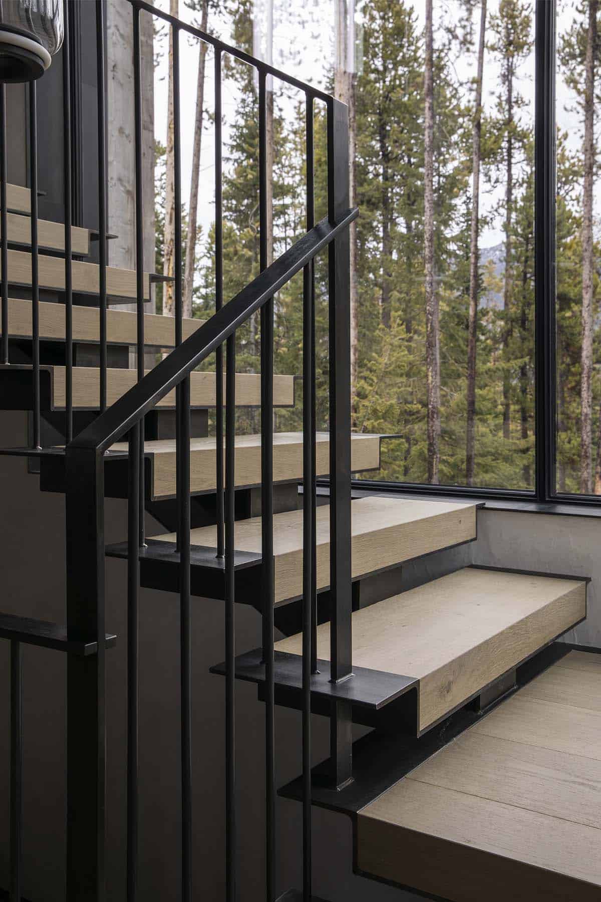 Close-up detail of floating oak stair treads with black steel stringers and vertical rod railing beside forest window