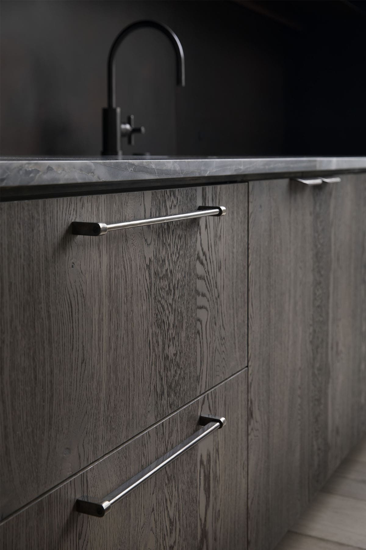 Close-up detail of dark oak drawer fronts with brushed nickel bar pulls and dark stone countertop