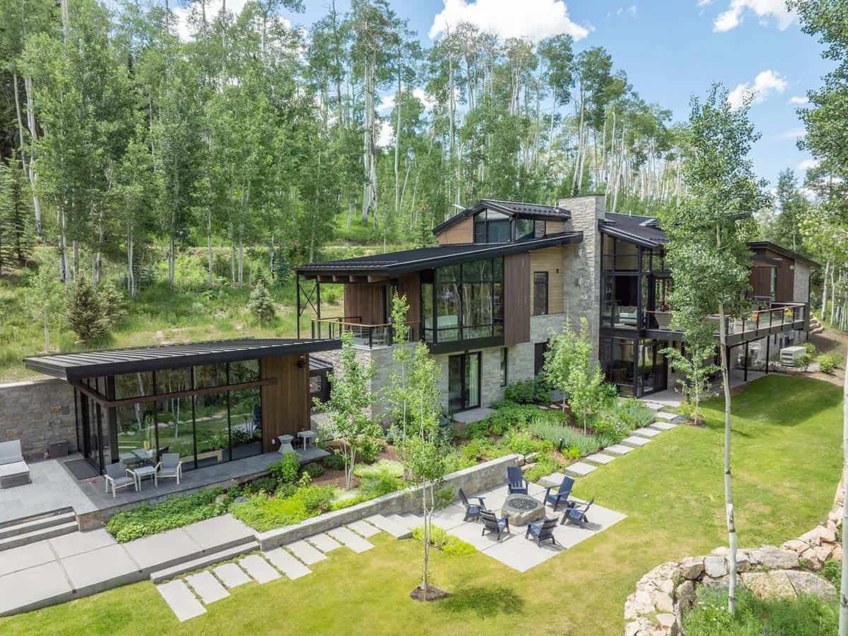 Aerial view of modern mountain home with stone, wood, and glass exterior surrounded by aspen trees