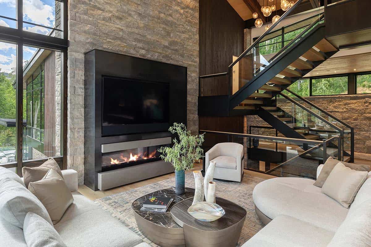 Living room with floor-to-ceiling stone fireplace, TV, floating staircase, and globe pendant lights