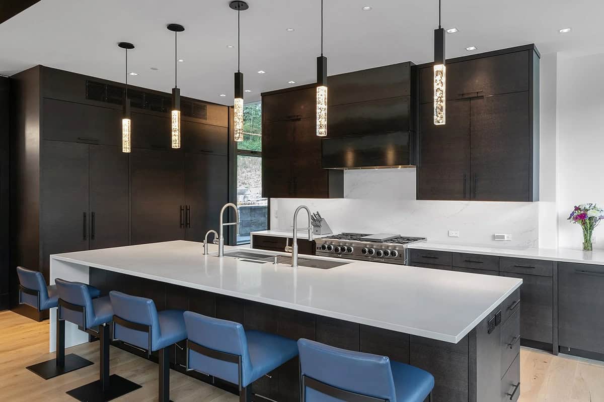 Chef's kitchen with large white island, dark wood cabinetry, professional range, and crystal pendant lights