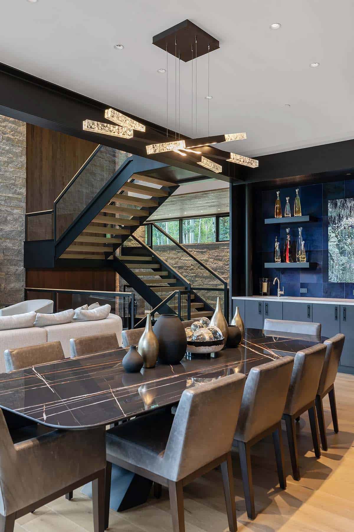 Dining area with black marble table, sculptural pendant light cluster, and adjacent wet bar
