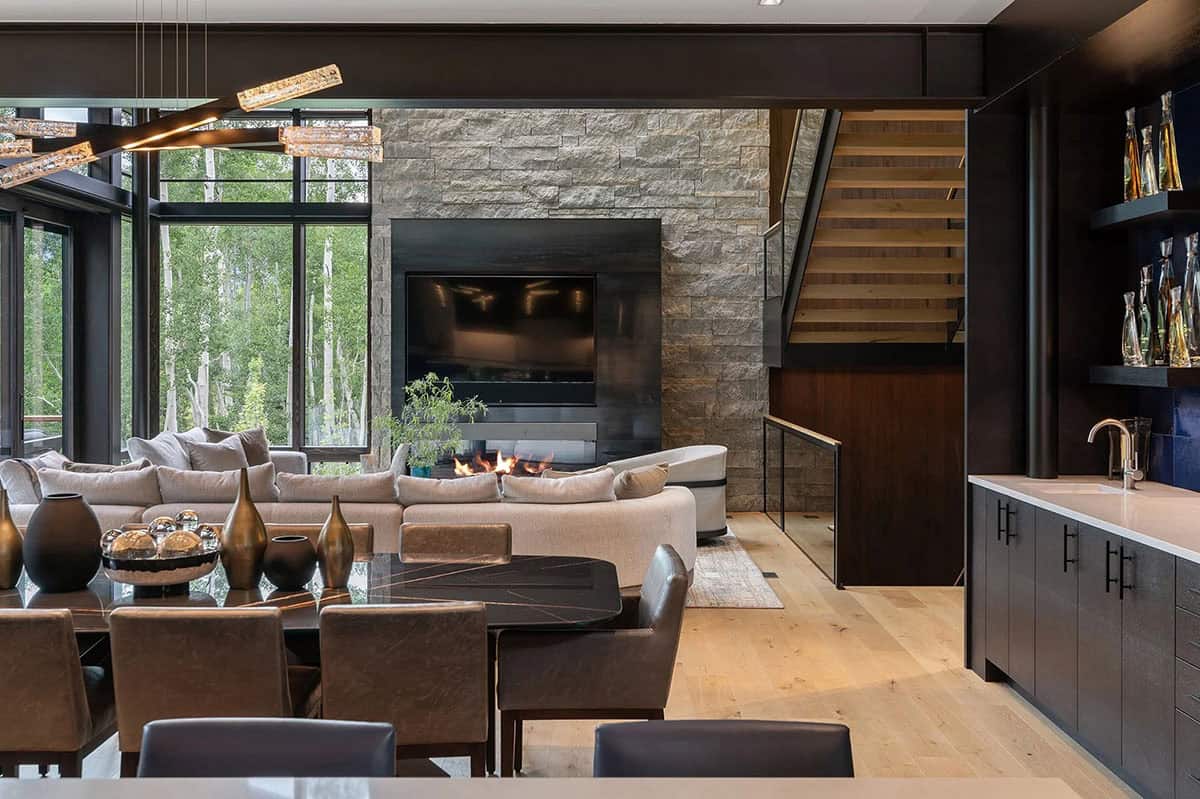 Open-plan great room connecting dining, living, and bar areas with stone fireplace and staircase