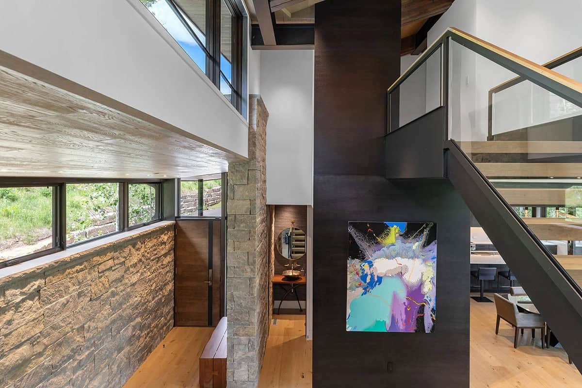 Foyer hallway with stone wall, abstract colorful artwork, powder room glimpse, and steel staircase