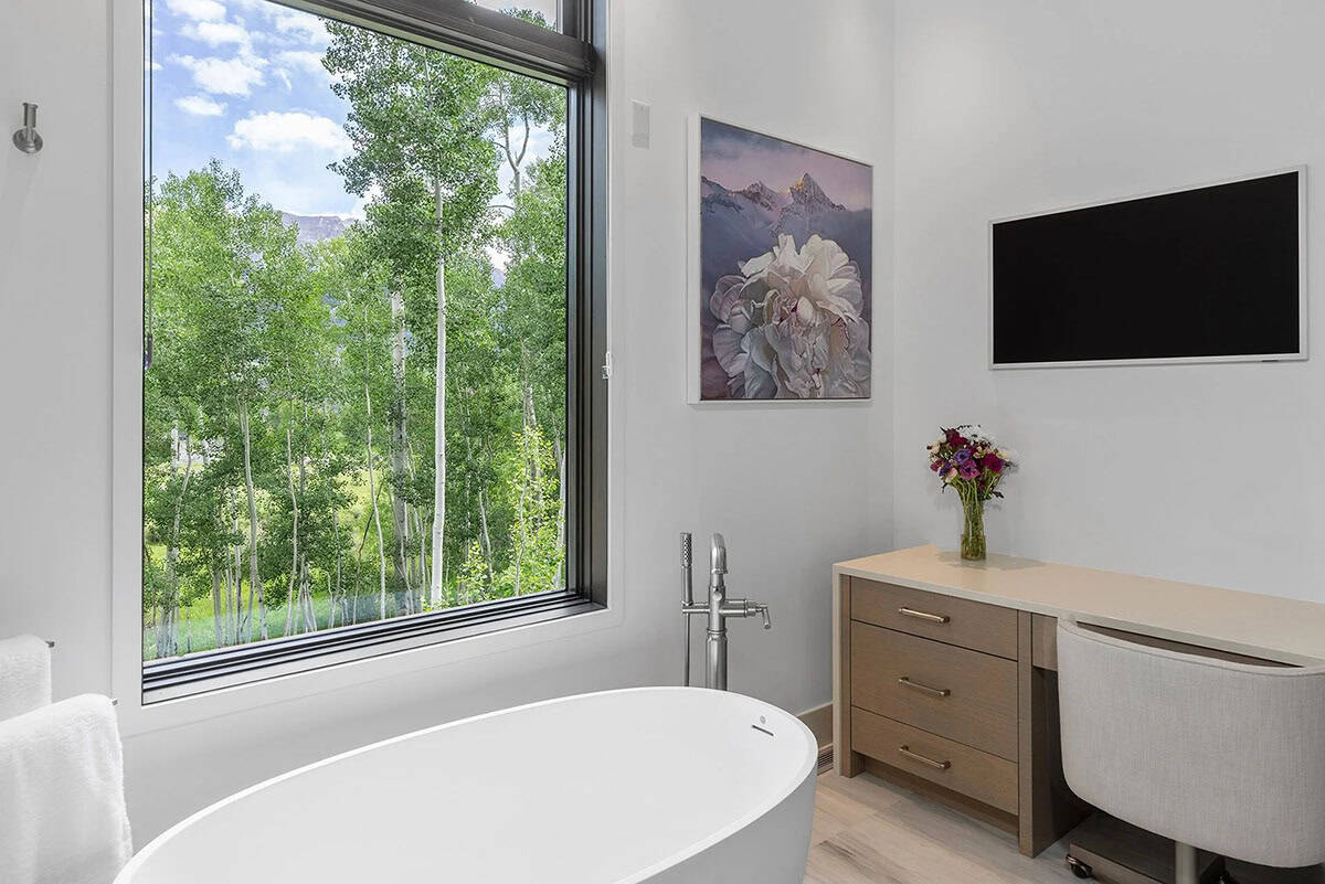 Primary bathroom with freestanding soaking tub, large window overlooking aspen grove, and mountain artwork