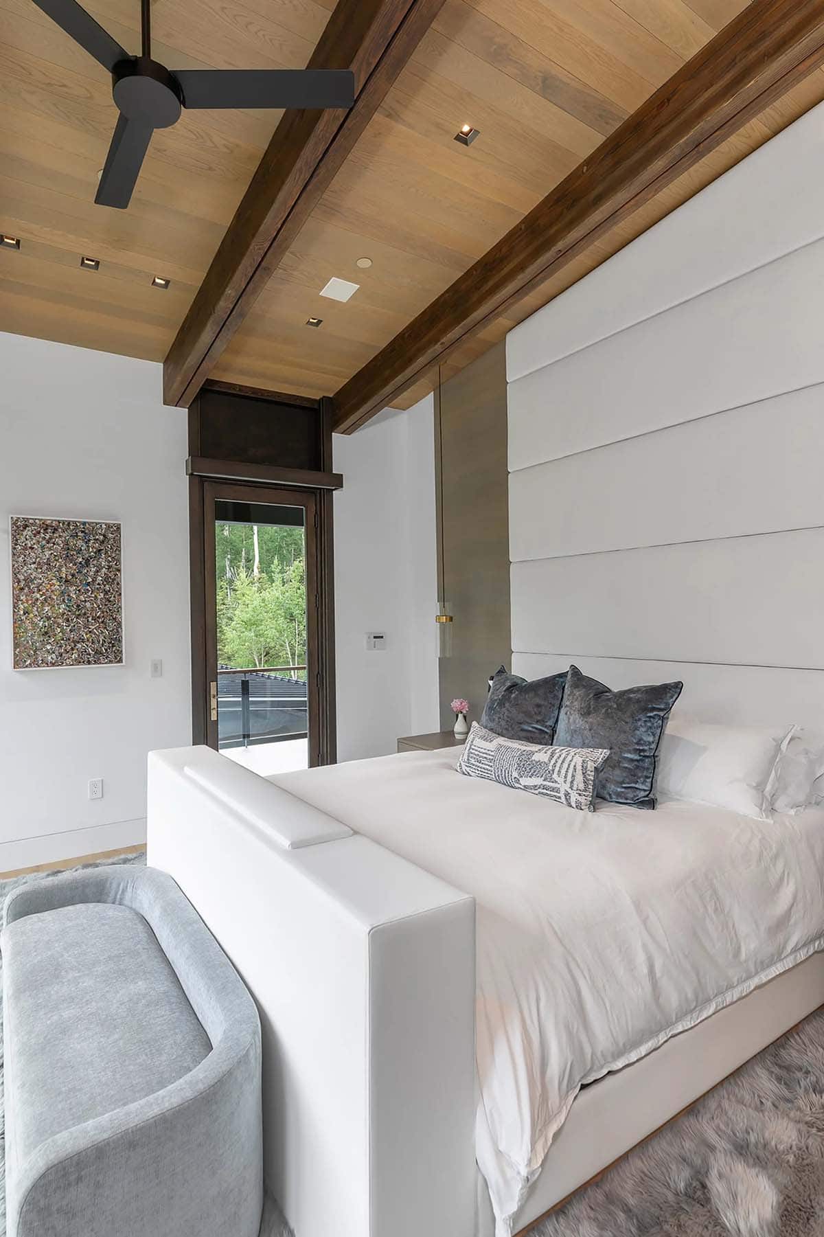 Primary bedroom with high upholstered headboard, wood beam ceiling, balcony door, and abstract artwork