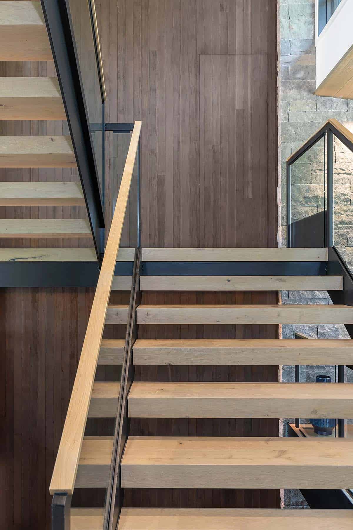 Close-up detail of open-riser staircase with light oak treads, black steel frame, and walnut wood-paneled wall