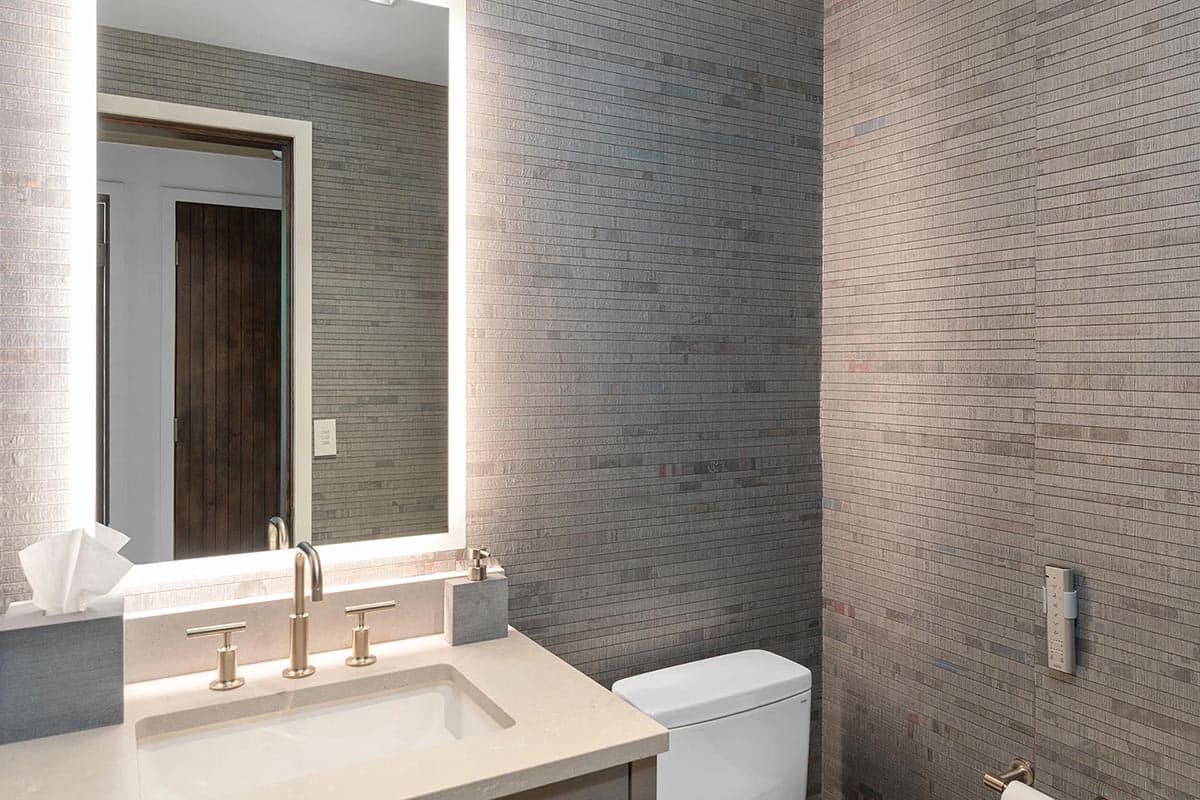 Guest bathroom with linear mosaic tile walls, backlit vanity mirror, quartz counter, and gold fixtures