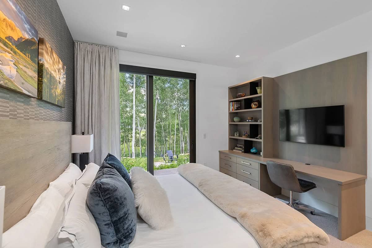 Guest bedroom with textured headboard wall, built-in shelving with TV, sliding glass door, and mountain painting