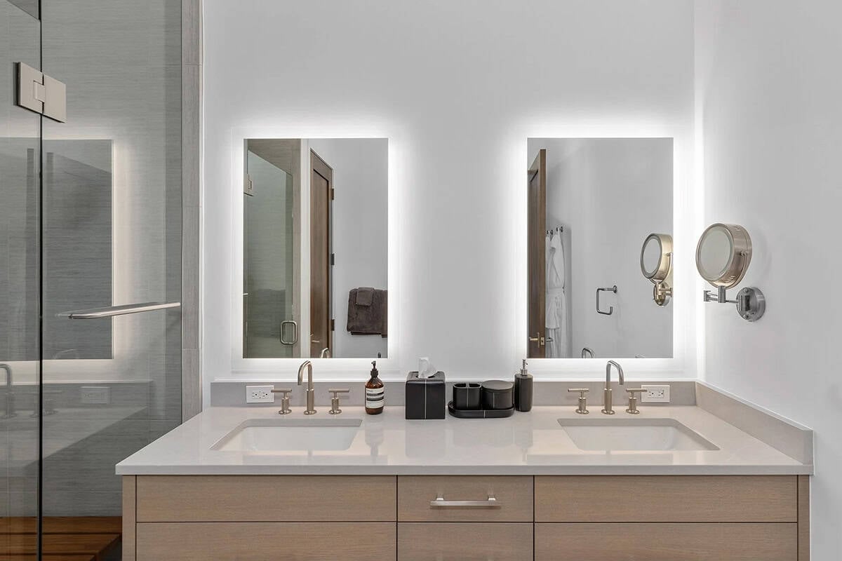 Guest bathroom with double backlit vanity mirrors, quartz double sink, and frameless glass shower