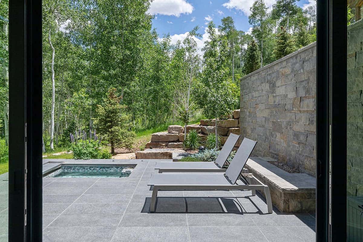 Lower patio viewed from interior with lounge chairs, mosaic-tiled plunge pool, stone retaining wall, and aspen forest