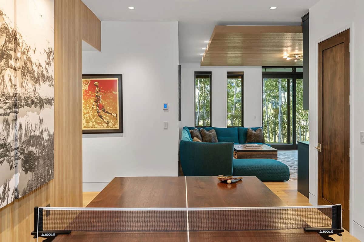 Lower-level game room with ping pong table, sports artwork, and teal sectional lounge area with aspen views