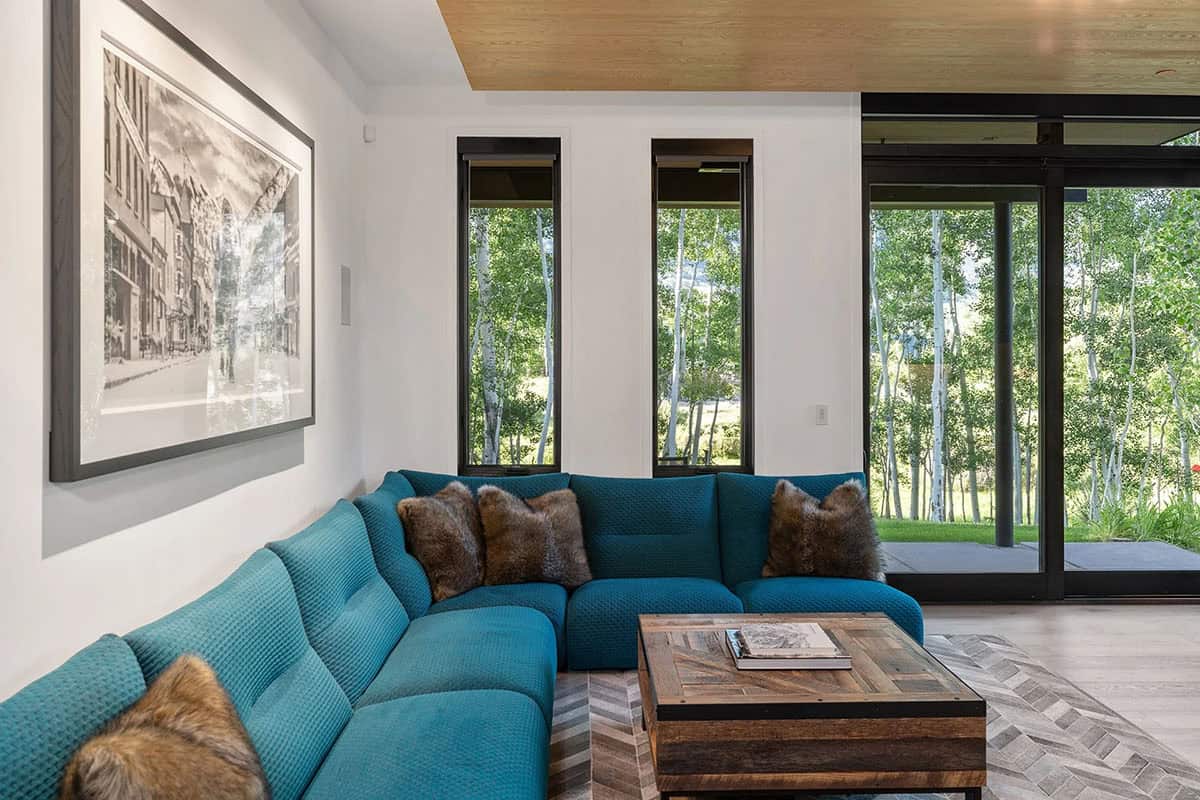 Lower-level lounge with teal sectional sofa, reclaimed wood coffee table, herringbone rug, and aspen forest views