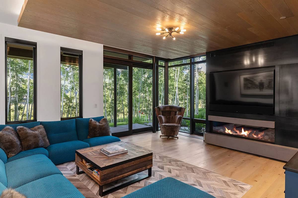 Lower-level family room with teal sectional, linear gas fireplace, black TV wall, and wraparound aspen views