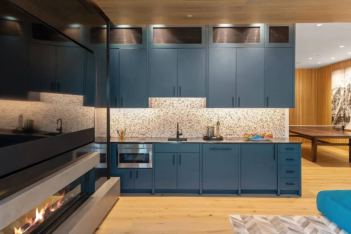 Lower-level kitchenette with slate blue cabinetry, mosaic tile backsplash, built-in microwave, and adjacent fireplace
