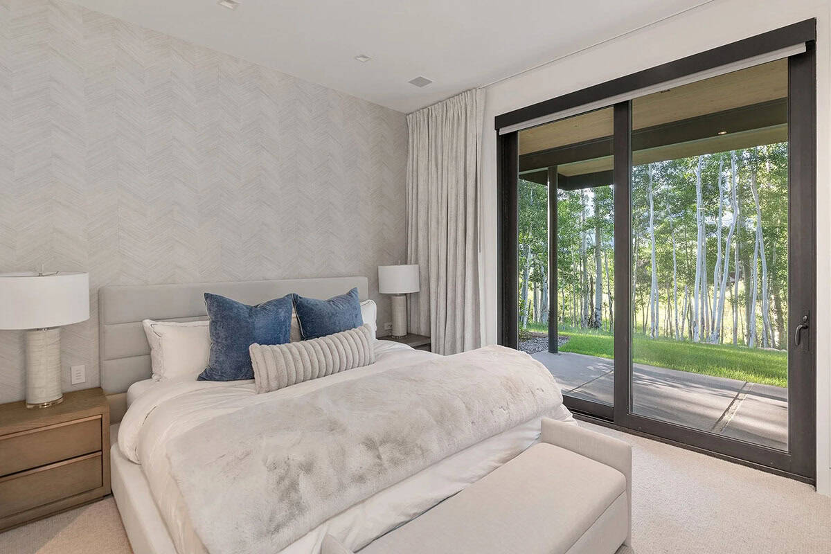 Guest bedroom with upholstered headboard, chevron wallpaper accent wall, blue velvet pillows, and sliding glass door to garden