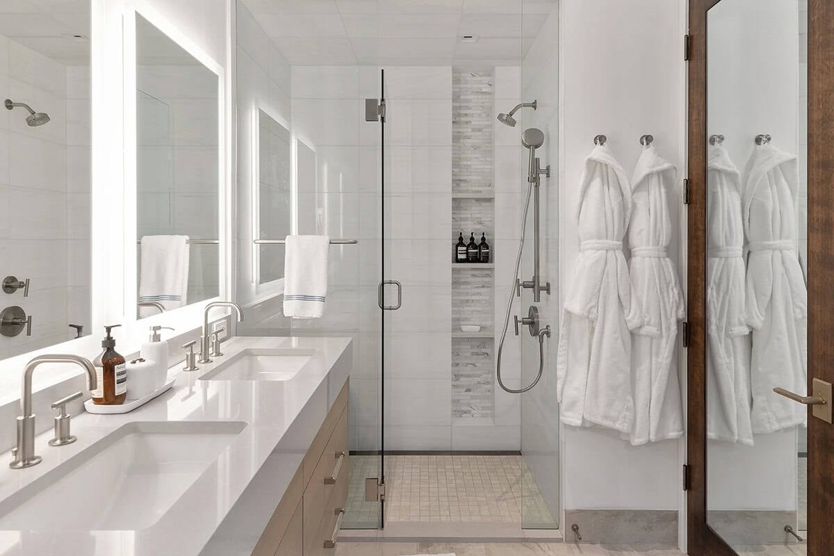Guest bathroom with double backlit vanity mirrors, frameless glass shower, white tile, and hanging robes