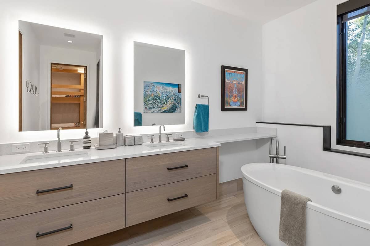 Guest bathroom with double backlit mirrors, floating wood vanity, freestanding soaking tub, and Telluride ski map artwork