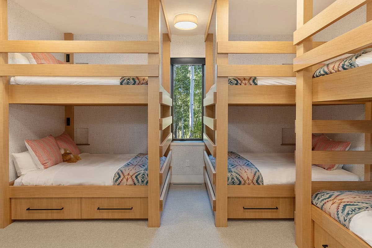 Bunk room with four built-in oak bunk beds, under-bed storage drawers, patterned bedding, and narrow aspen-view window