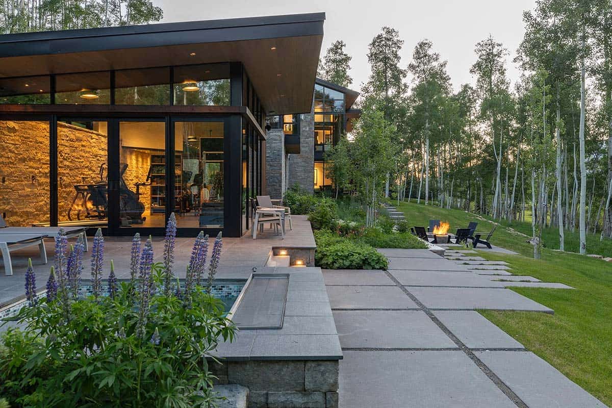 Dusk view of gym pavilion and terraced grounds with hot tub edge, lupines, flagstone path, fire pit, and aspen grove
