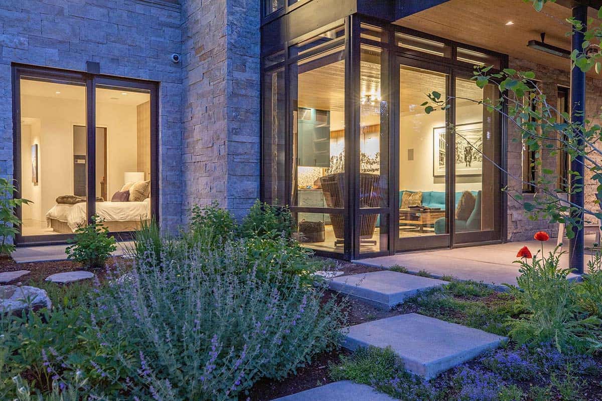 Evening exterior showing lit bedroom and lounge through glass walls, stone facade, and stepping stone garden path
