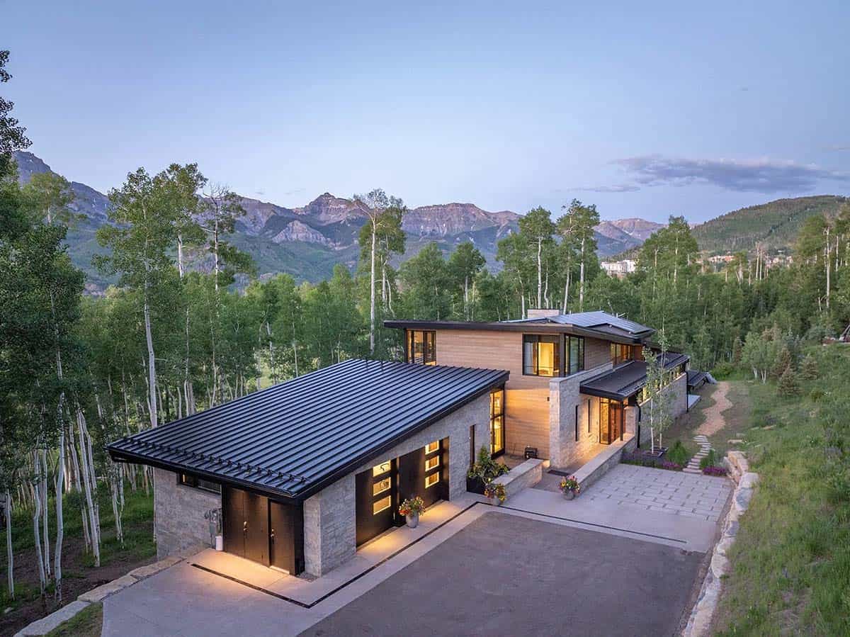 Aerial dusk view of modern mountain home with black standing-seam roof, stone and wood facade, and San Juan Mountain backdrop