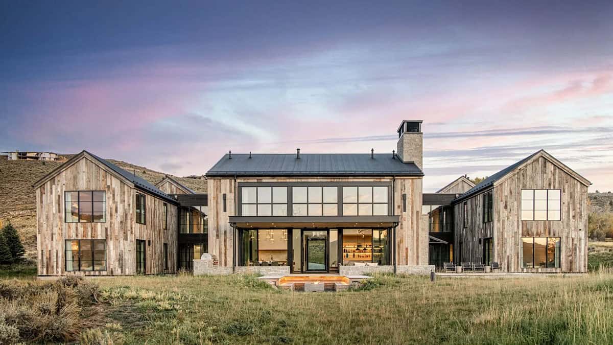 Reclaimed wood and steel mountain home at dusk with glowing interiors in Utah