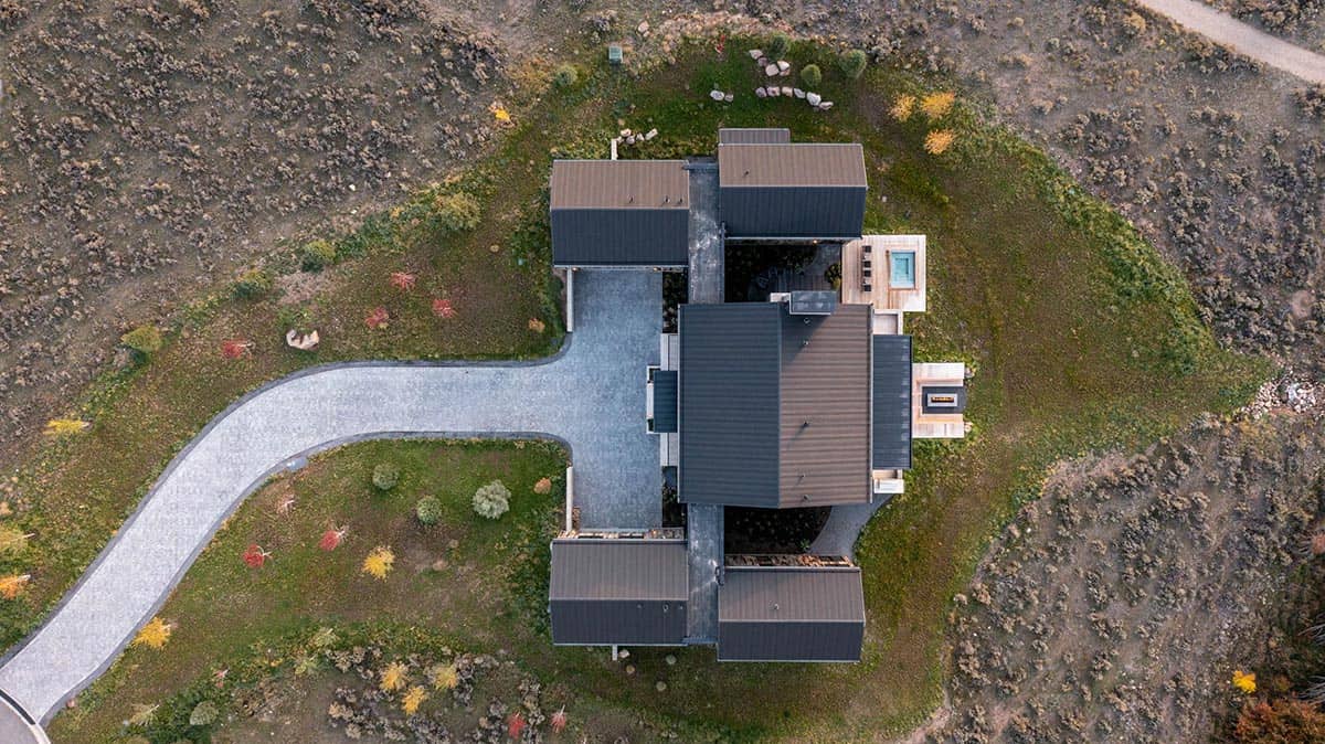Aerial overhead view of multi-gabled mountain home with dark metal roofs and curved driveway