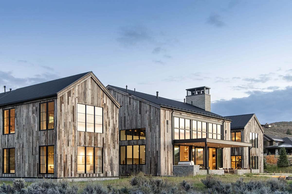 Side elevation of illuminated reclaimed wood home with floor-to-ceiling steel windows at dusk