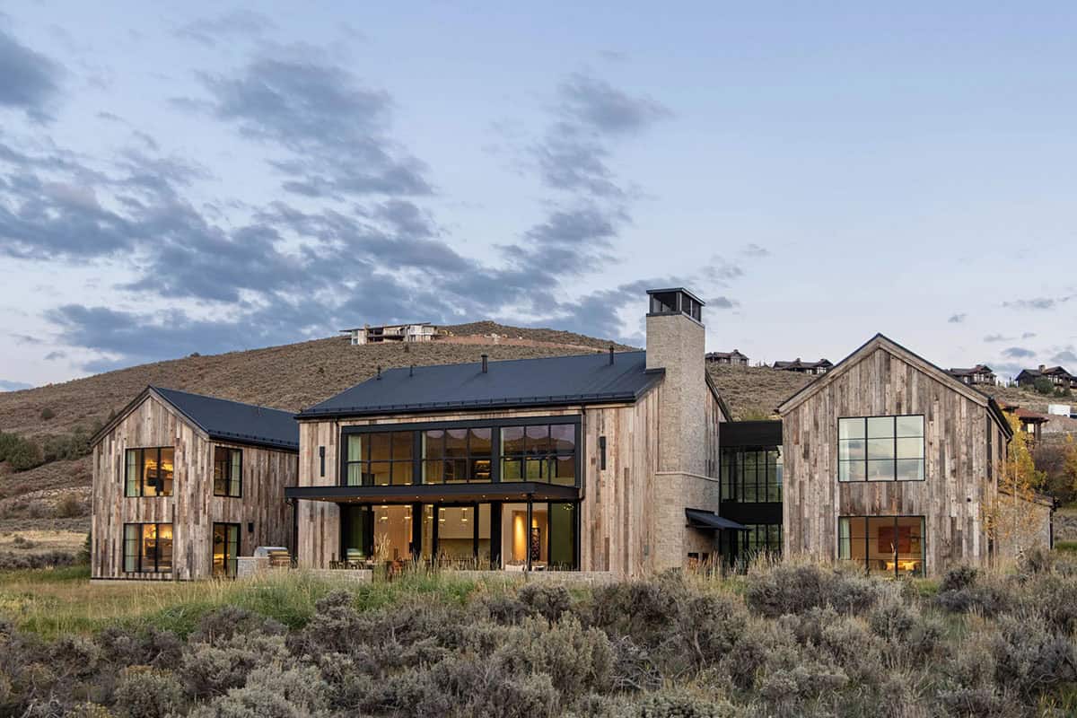 Rear elevation of reclaimed wood and stone mountain home glowing at dusk