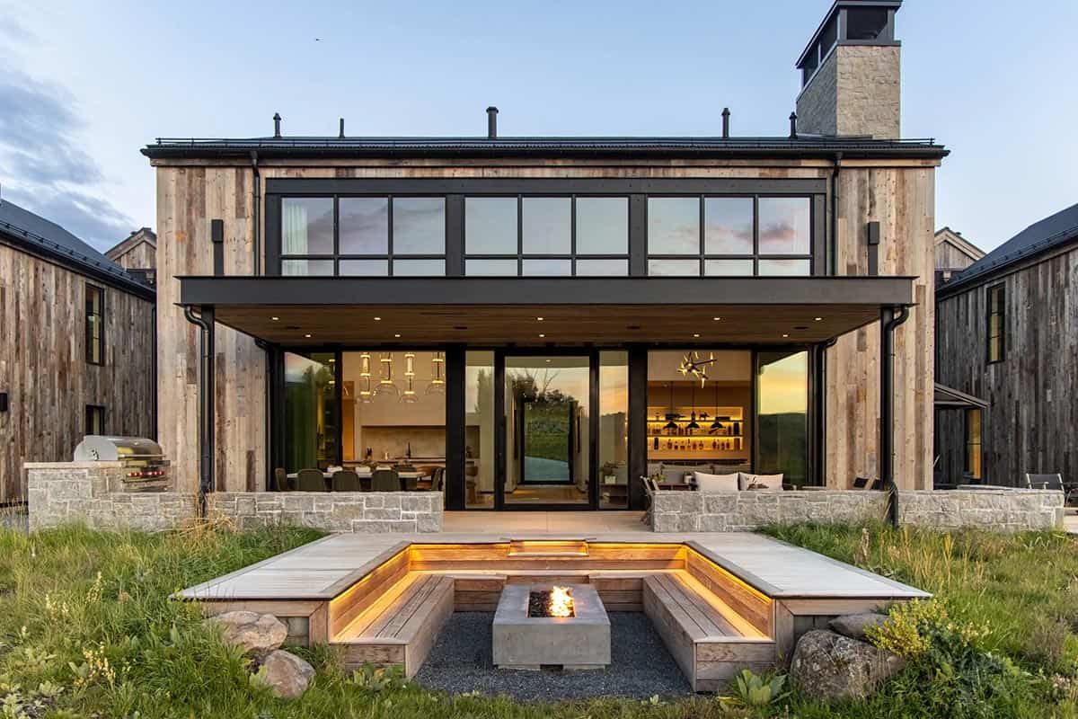 Sunken fire pit terrace with built-in wood benches at rear of mountain home at dusk
