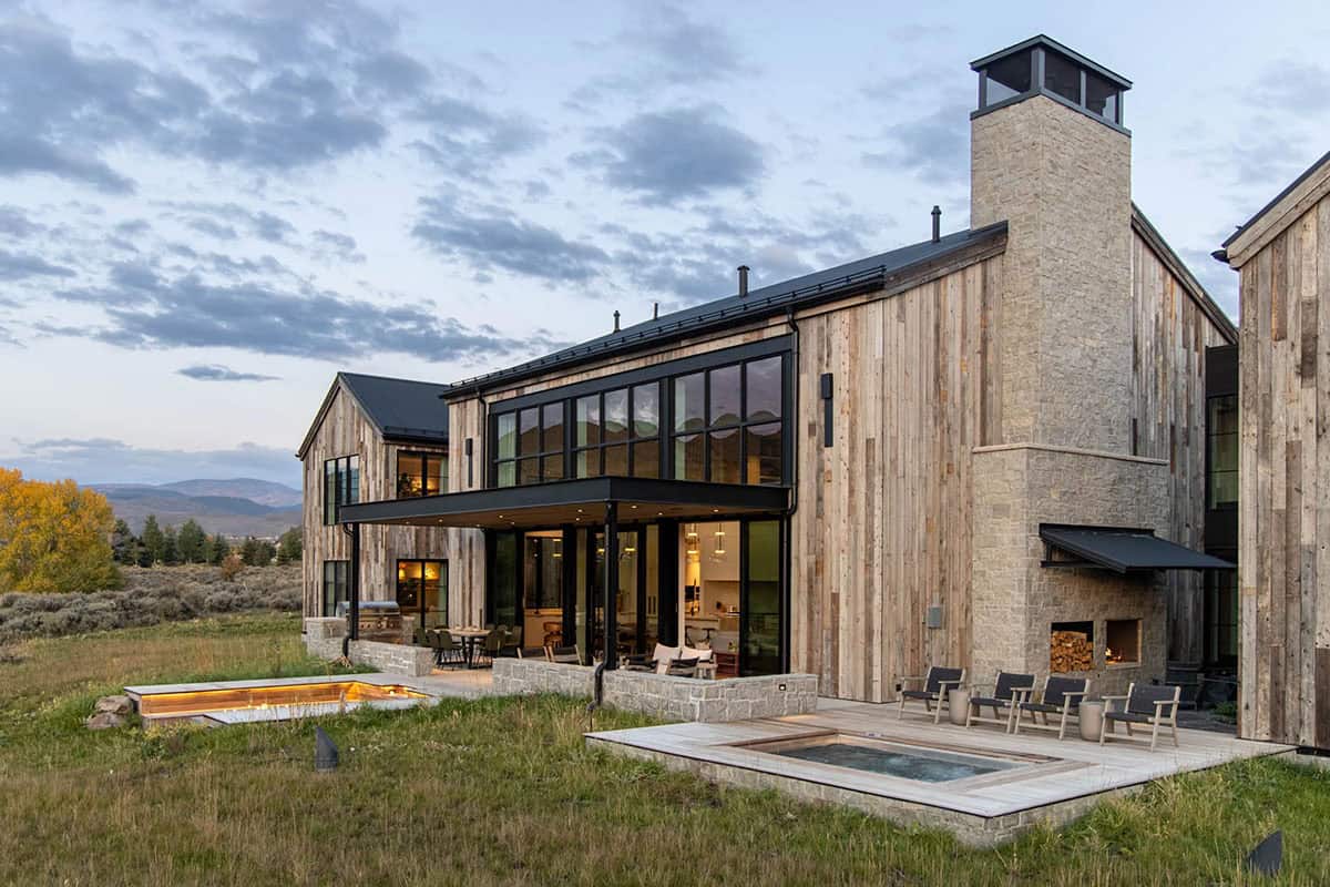Rear view of mountain home showing hot tub deck, outdoor fireplace, and covered terrace at dusk
