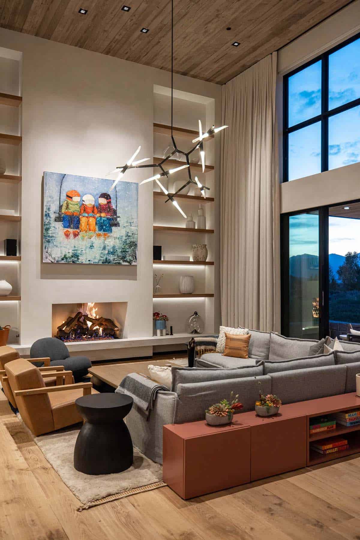 Two-story living room with plaster fireplace, floating shelves, and branch-form chandelier