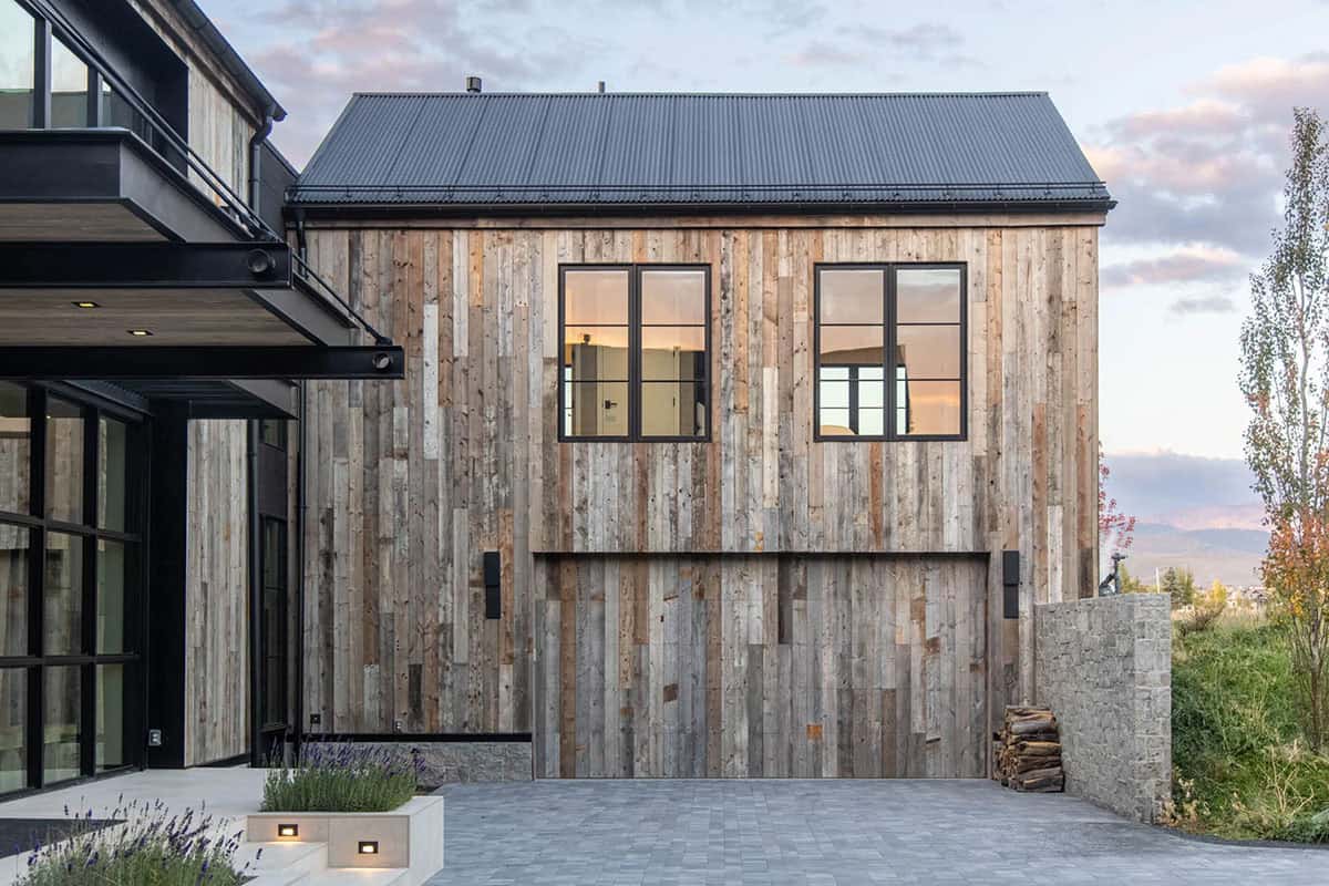 Reclaimed wood garage wing with sliding barn door and corrugated metal roof at dusk