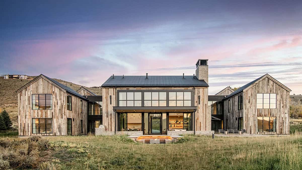 Twilight rear elevation of reclaimed wood mountain home with sunken fire pit and open living area