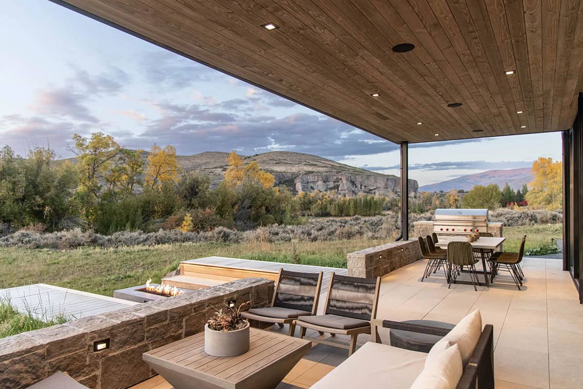 Covered outdoor patio with stone retaining wall, fire pit, dining area, and mountain views at sunset