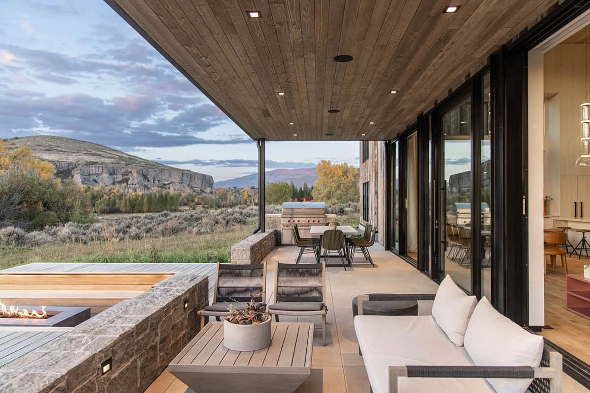 Modern covered porch with sliding glass doors, outdoor sofa, and sweeping canyon and mountain views