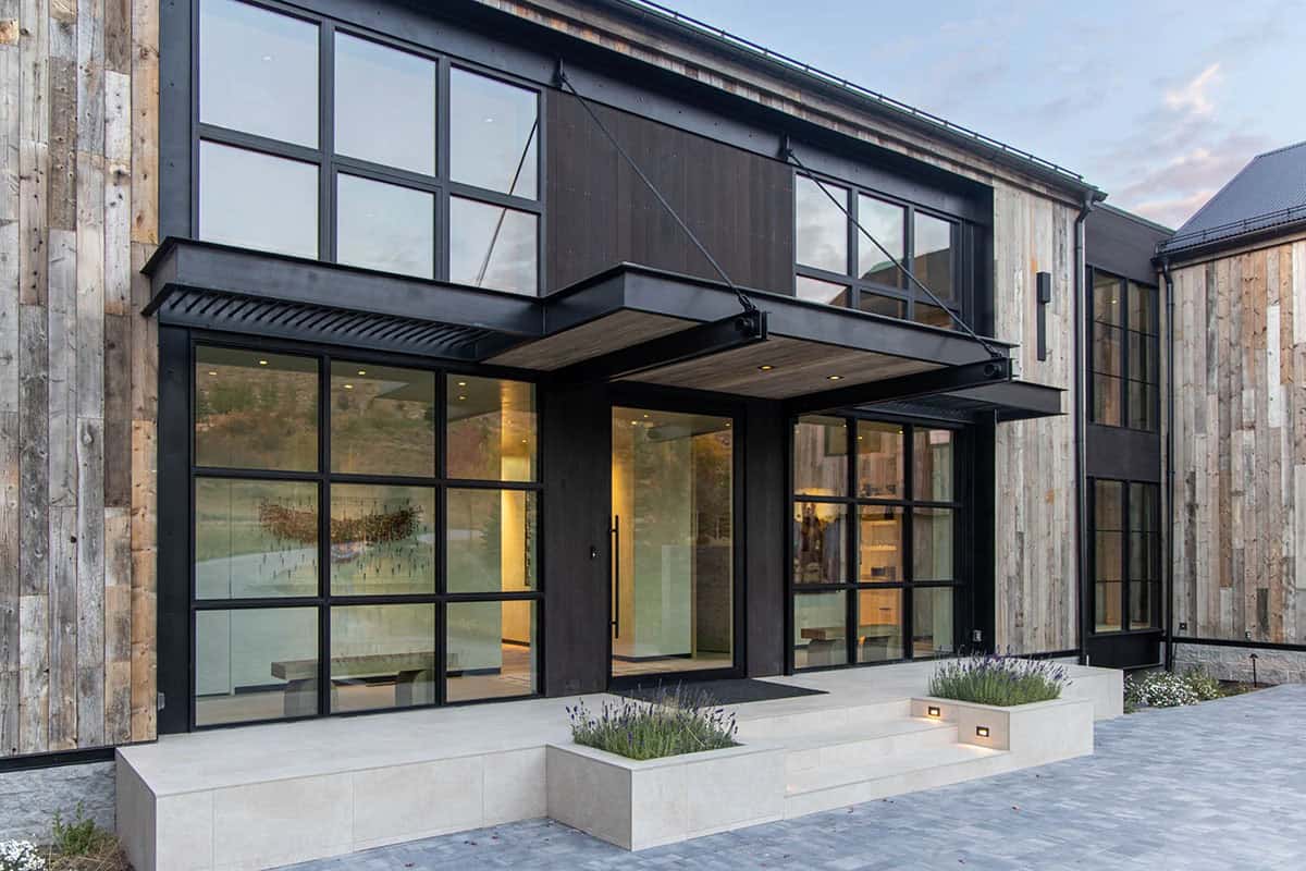 Modern mountain home exterior with reclaimed wood siding, black steel-framed windows, and cantilevered entry canopy