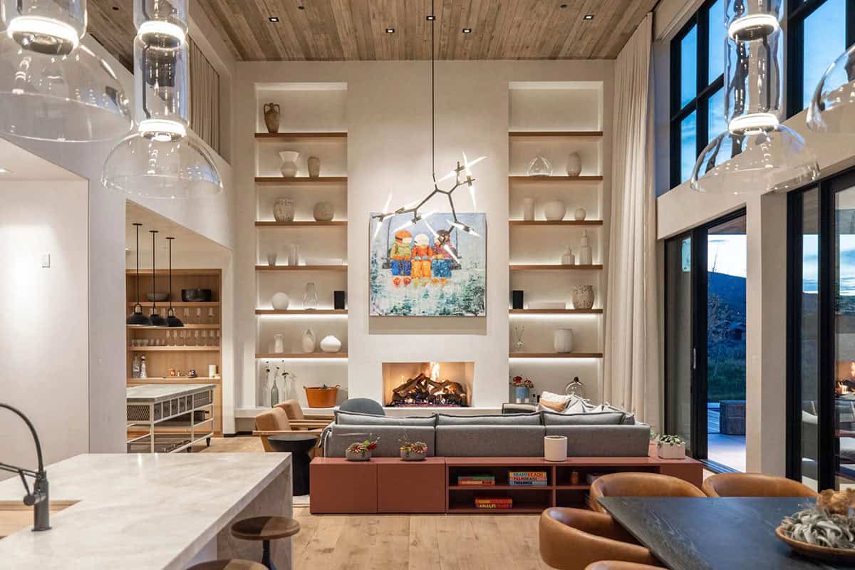 Double-height living room with floor-to-ceiling bookshelves, wood-burning fireplace, and branching chandelier