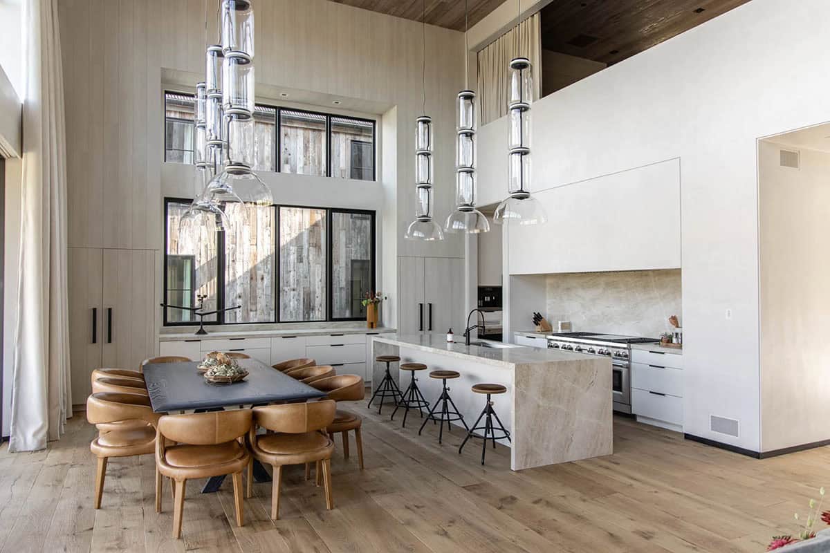 Open-plan kitchen and dining area with double-height ceilings, pendant glass lights, and reclaimed wood accent wall